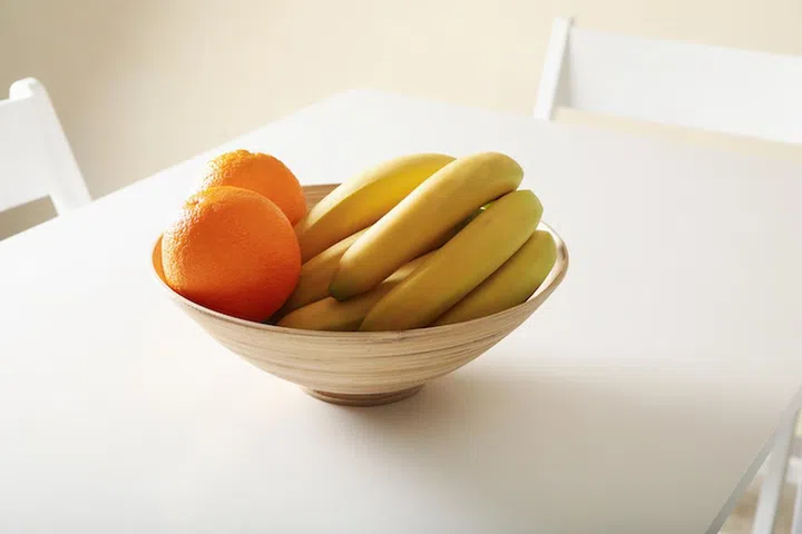 Bowl with oranges and bananas on white table