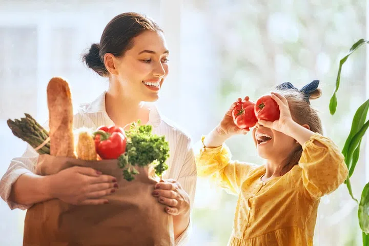 Family shopping. Mother and her daughter are holding grocery shopping bag with vegetables.