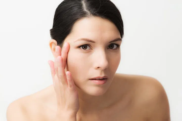 Portrait of a sexy brunette Caucasian young woman looking in the mirror, observing facial wrinkles, first sign of ageing