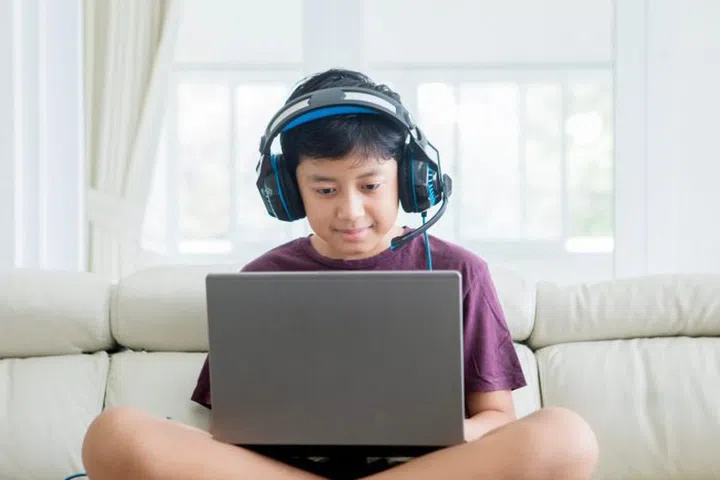 Picture of Asian preteen boy sitting on the couch while using a laptop and headphones at home