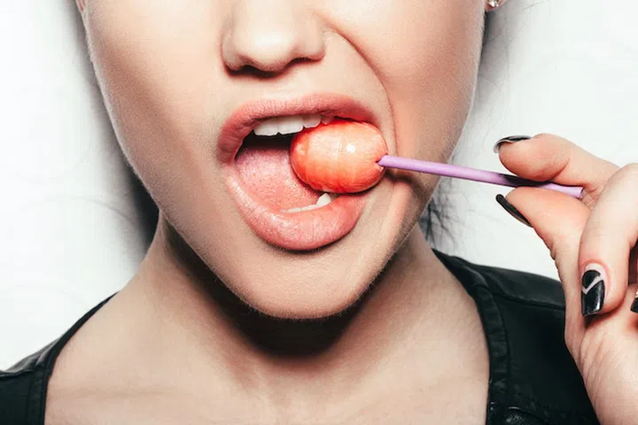 Woman licking a red shiny lollipop. Close up against white background, not isolated