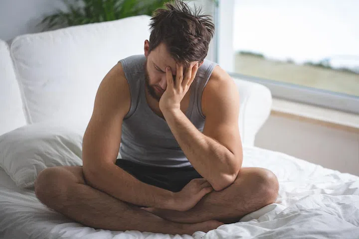Young worried man with insomnia sitting on bed in the morning
