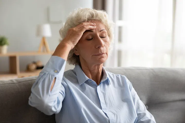 Upset senior elder lady touching forehead feeling dizzy unwell headache pain concept, sad tired old adult grandma suffering from hypertension, migraine, mental problem or fatigue sit on sofa at home
