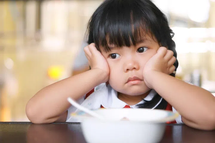 Asian children cute or kid girl student anorexia or sad with vacant and prop up or hand to cheek on food table for breakfast before going to school for study