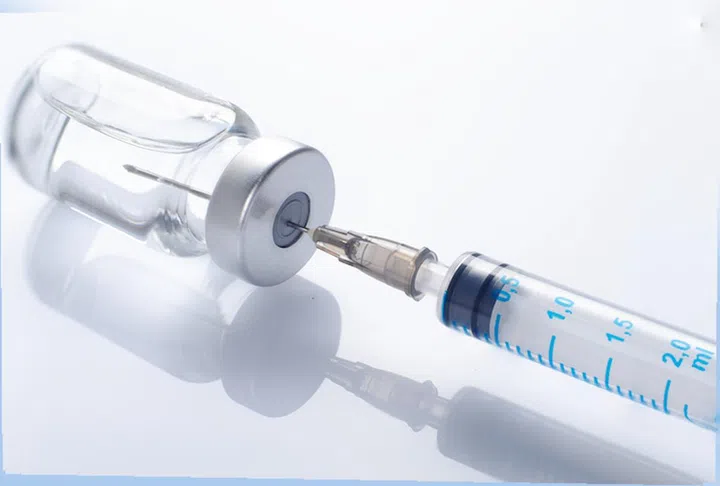 Just opened vaccine vial with inserted syringe for injection treatment on medical table. Vaccination or immunization care concept background.