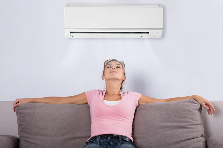Happy Young Woman Holding Remote Control Relaxing Under The Air Conditioner