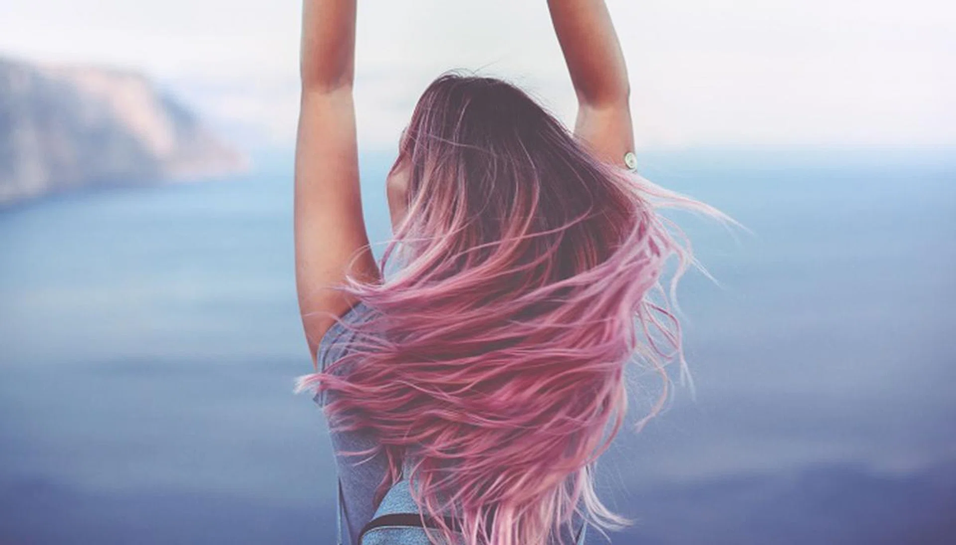 Woman with pink hair standing on the mountain top over blue sea view, photo toned