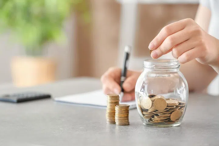 Woman putting coins into glass jar on table. Savings concept