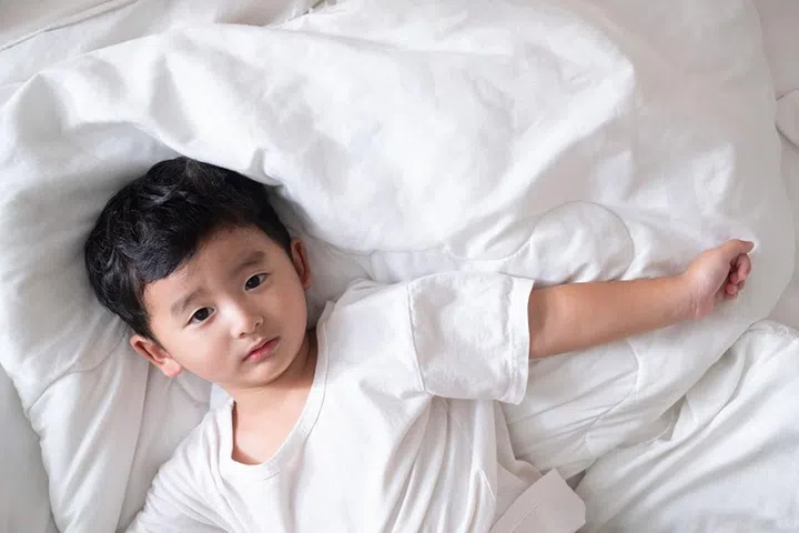 3 years old little sick or illness Asian boy at home on the bed, sad kid laying resting on white bed with pillow and blanket, top view with copy space for add text.