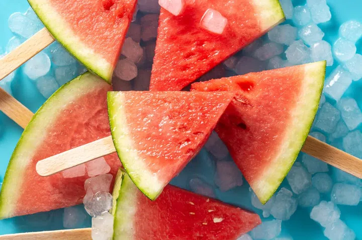 Watermelon slices popsicles and ice on blue background
