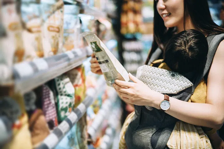 Young Asian mother grocery shopping with little daughter and choosing for organic baby food in the supermarket