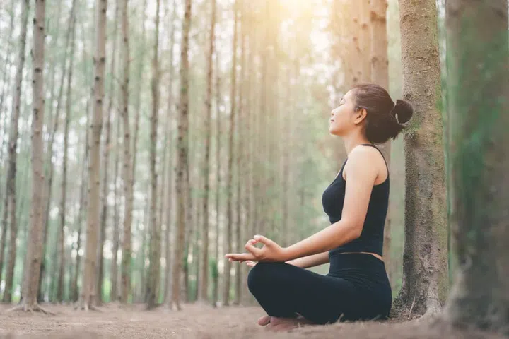 Young female relaxes in yoga pose in green nature