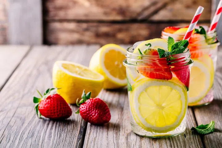 Lemon and strawberry lemonade in glass mason jars on a wooden background. A refreshing summer drink.