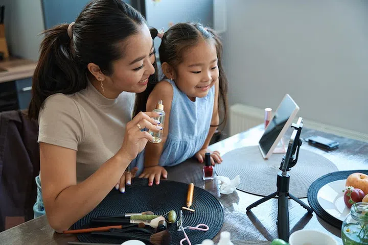 Happy asian mom and daughter having fun at home doing makeup in a bright room