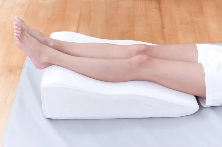 A woman's legs lay down on a pillow for relaxing and preventing varicose vein