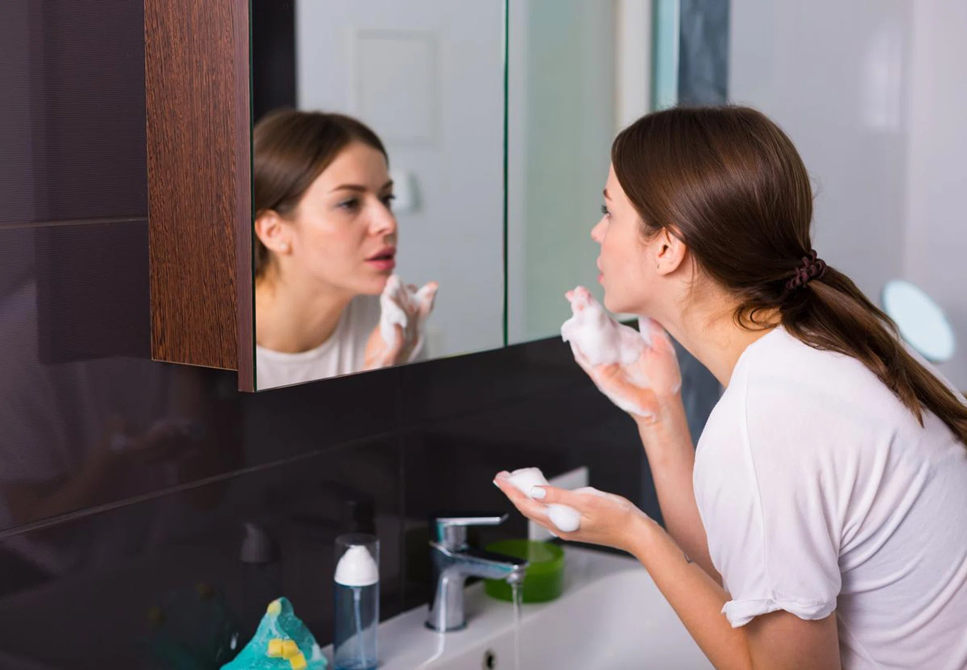 Woman washing up her face with foam cleanser in the morning