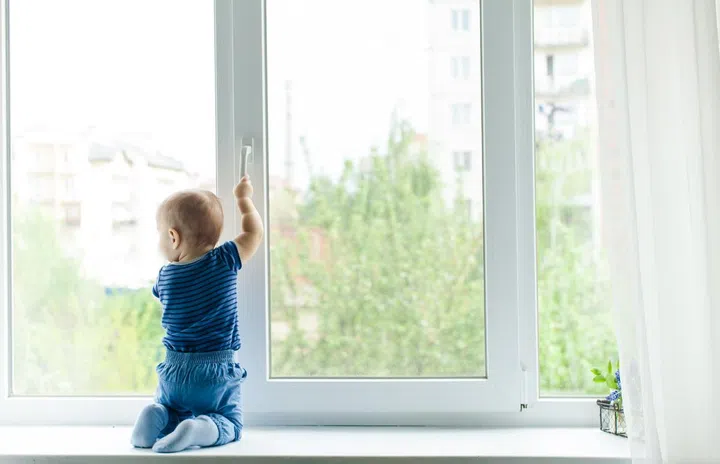 Baby boy sit on the windowsill and trying to open the window pulling its handle