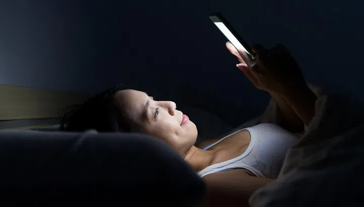 Woman use of mobile phone and lying on bed at night