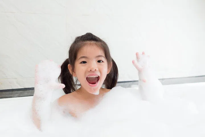 lovely sweet little daughter holding bubble in hands enjoying playing time on bathtub at home and looking at camera laughing.