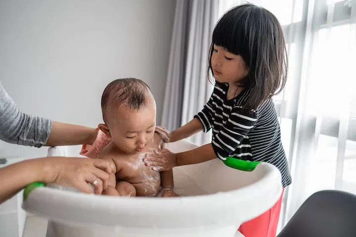 helpful sister wash her baby brother while taking a bath time in basin