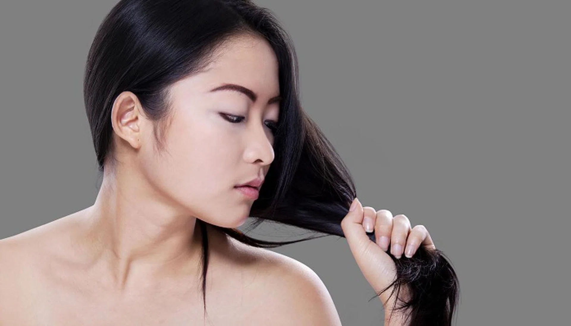 49250716 - lovely young woman with perfect skin looking at her black hair against grey background