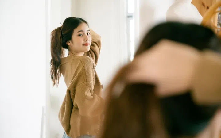Young beautiful asian woman happily dressed in front of the mirror. She looks good and has confidence in herself