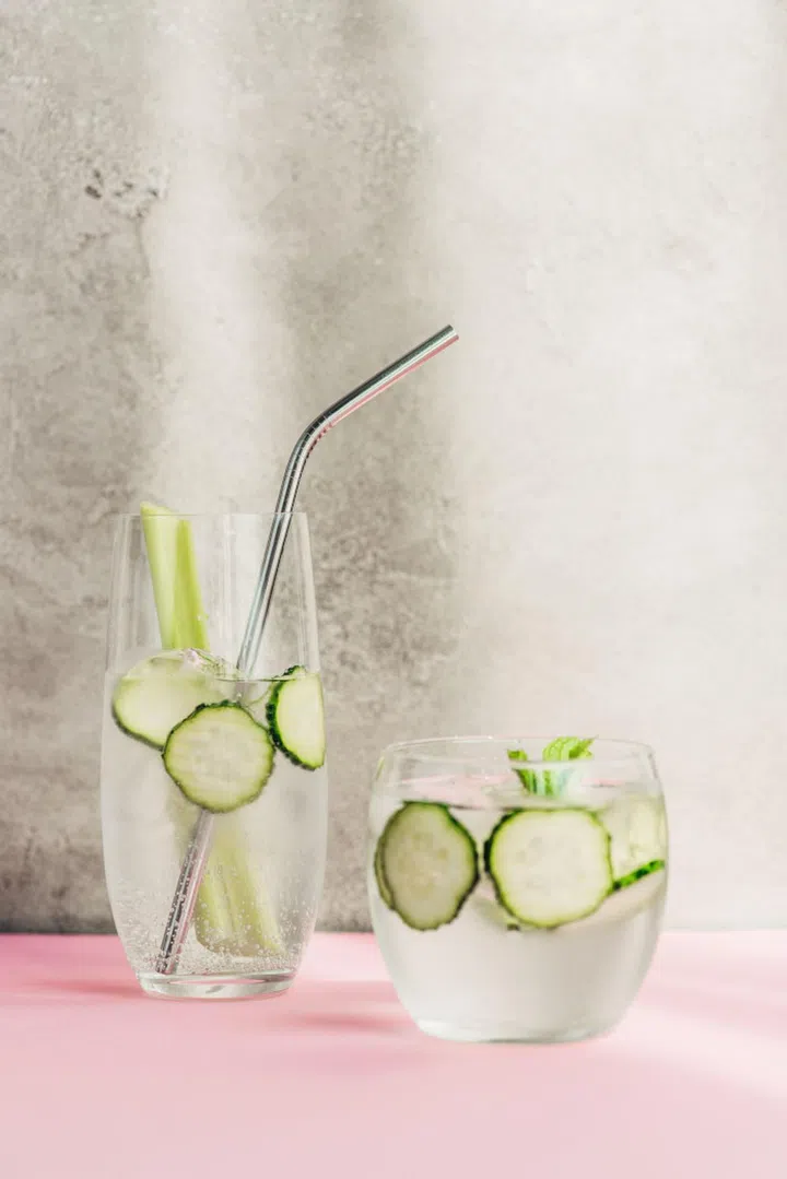 fresh lemonade with ice, celery, straw and cucumber slices in sunlight