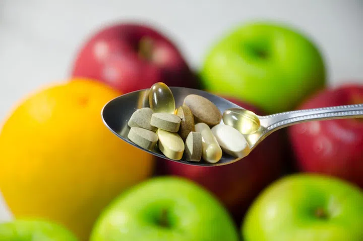 Assorted vitamins and nutritional supplements in serving spoon. on blur colorful fruits background