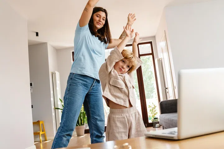 Photo of young positive beautiful woman at home with her son exercising while looking at laptop computer