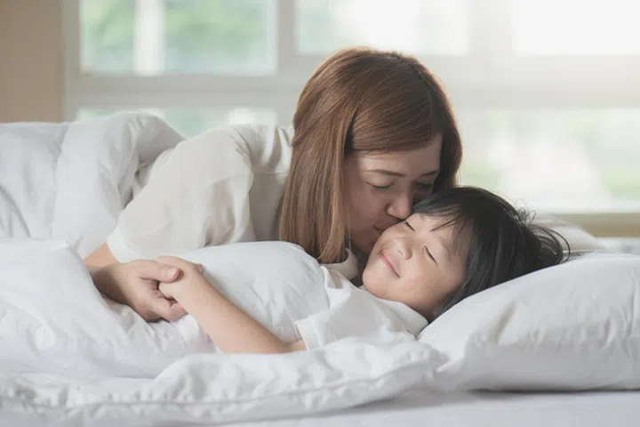 Asian mother  kissing her son on white bed