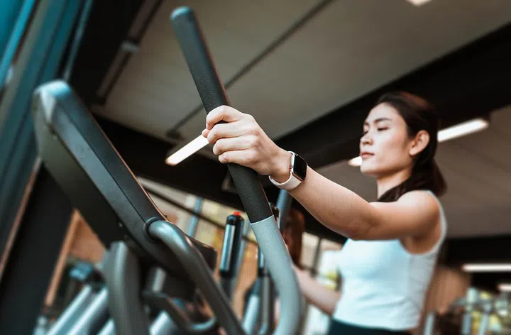 Young fitness girl walking on the elliptical machine at the gym