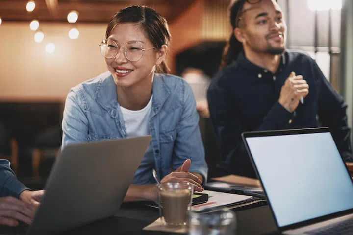 Smiling young Asian businesswoman meeting with a diverse group of colleagues around a table in an office