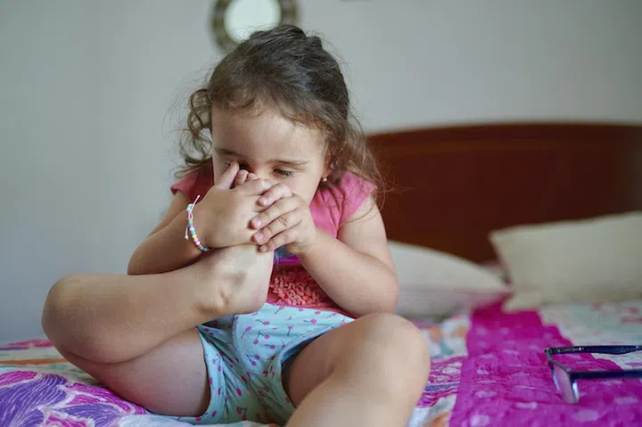Little girl smelling her foot at home
