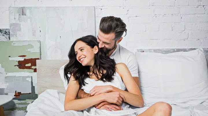 joyful young couple hugging while having fun in bed