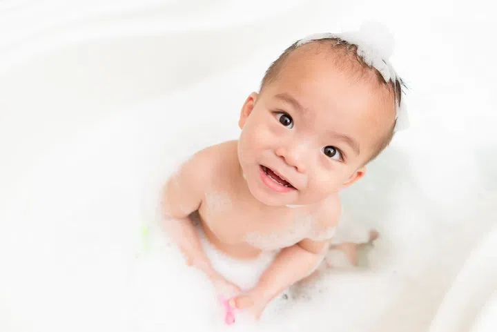 high angle view photo of pleasantly handsome little boy kid on bathroom sitting in bathtub playing foam bubble water and washing body at relaxing time.