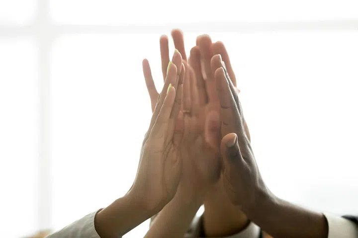Motivated multiracial business team join hands palms together, black and white diverse people group give high five as concept of successful teamwork and help support unity in common goal achievement