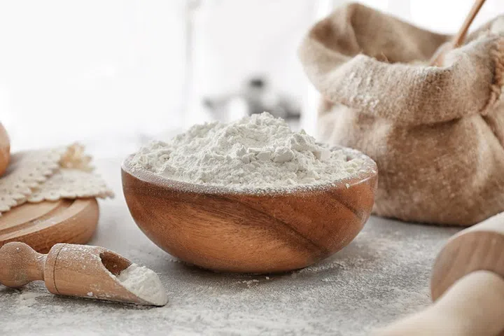 Bowl of wheat flour on blurred background