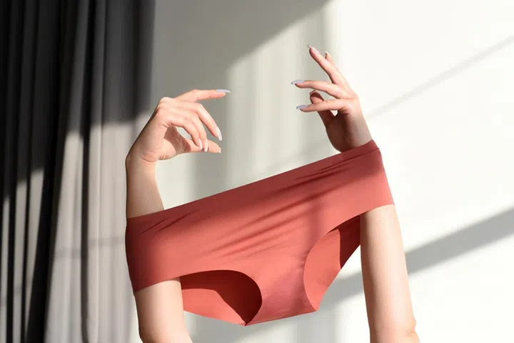 Seamless female panties in the hands of the girl. White background with sun shadow.