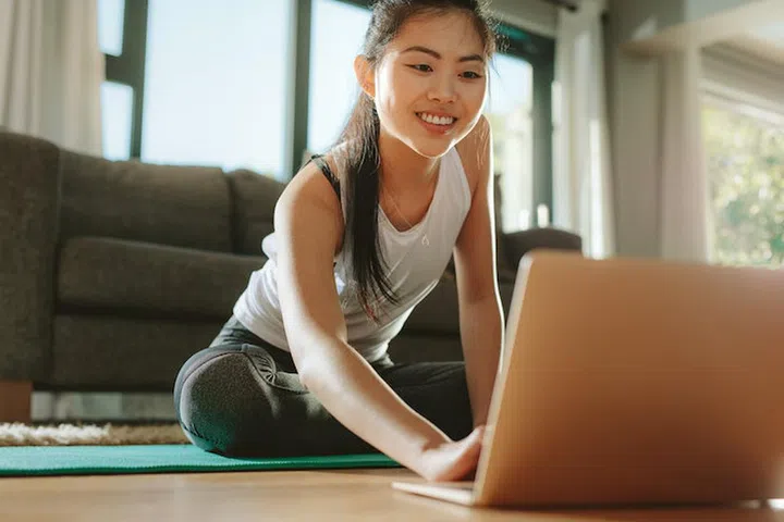 Woman using laptop while exercising at home. Female in sportswear sitting on floor and watching exercise video for her workout.