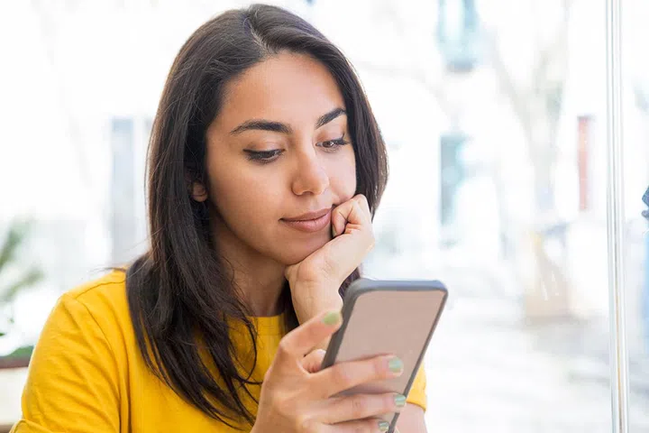 Content beautiful young woman using smartphone. Lady holding mobile phone and texting message with blurred view in background. Communication concept. Front view.