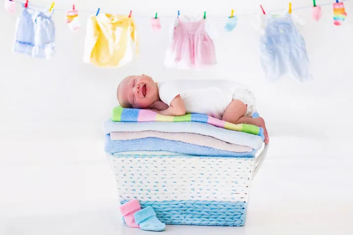 Newborn baby on a pile of clean dry towels. New born child after bath in a towel. Family washing clothes. Kids wear hanging on a line. Infant apparel, textile for children. Smiling boy after shower. 