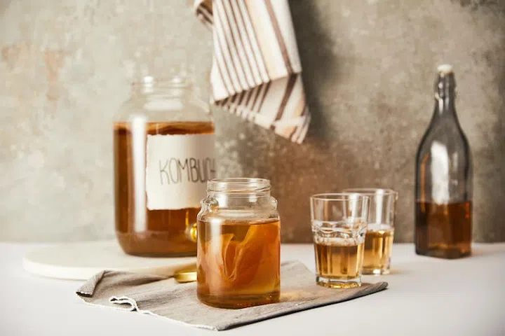 selective focus of jar with kombucha near glasses on textured grey background with striped napkin