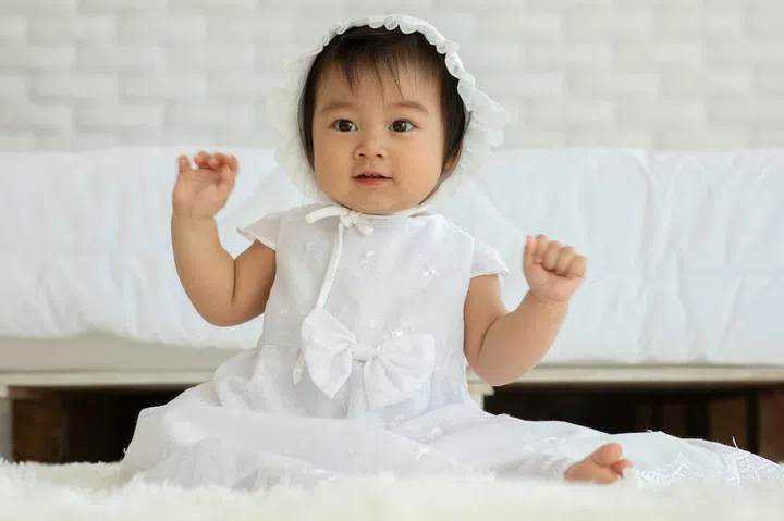 Cute Sweet Adorable Asian Baby wearing white dress sitting on Carpet smiling and playing with happiness emotional in cozy bedroom,Healthy Baby Concept