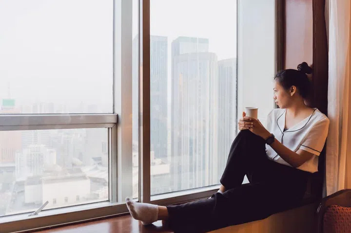 Asian woman holding coffee cup in bedroom looking out at window.Happy & smiling during the quarantine crisis of the covid19. Concept of social distancing at home in epidemic situation of corona virus.