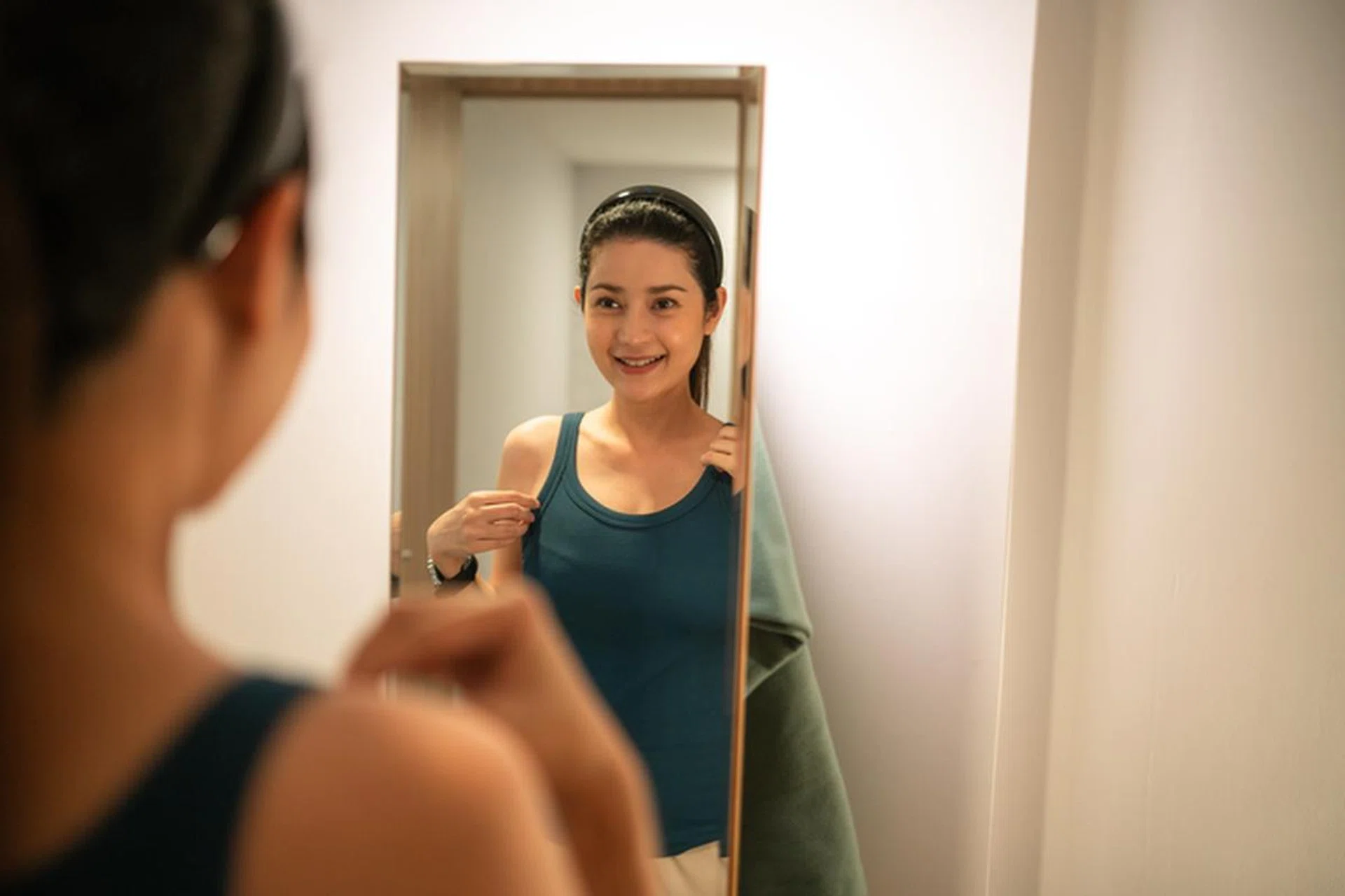 Asian happy Customer woman try on shirt clothing, singlet and looking at mirror. online shopping