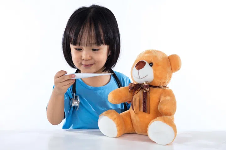 Happy Asian Chinese little girl examine teddy bear with thermometer in isolated white background.