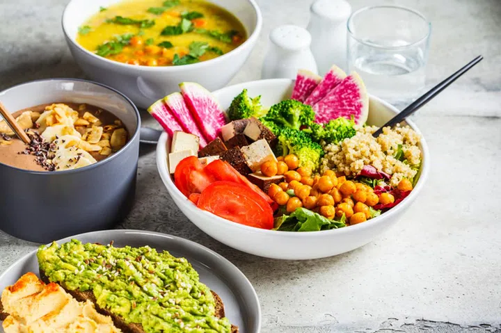 Vegan lunch table. Chocolate smoothie bowl, Buddha bowl with tofu, chickpeas and quinoa, lentil soup and toasts on a gray background.