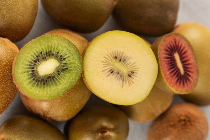 Different varieties of kiwi lie in a pile on the table. Halves of red, yellow and green kiwi. Fruit varieties.