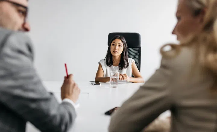 A promising young woman is having a job interview in a bright and simple office. She is trying to impress her possible future employers. Horizontal daylight indoor photo.