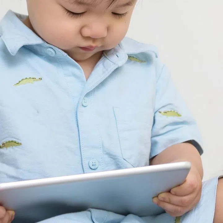 Closeup cute asian kid look at the tablet at home on gray carpet with doll and colorful ball and cement wall textured background with copy space